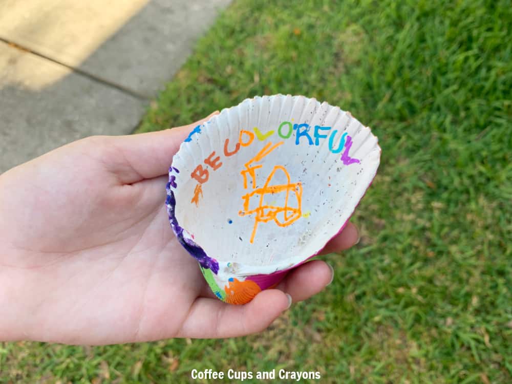 child holding a painted seashell with a message written inside